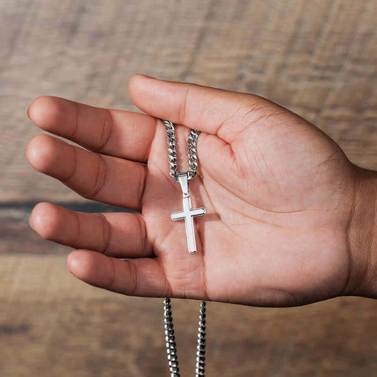 Hand holding a personalized cross keepsake graduation necklace, symbolizing love and strength.