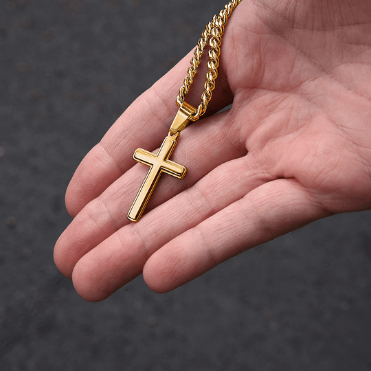 A hand holding a gold cross pendant on a Cuban link necklace, a meaningful milestone gift for loved ones.